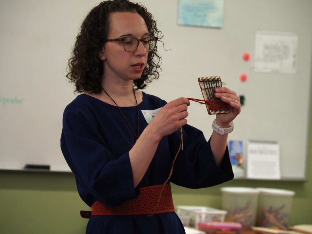 Professor Regina Burkholder demonstrating how to weave on a hand-held loom.